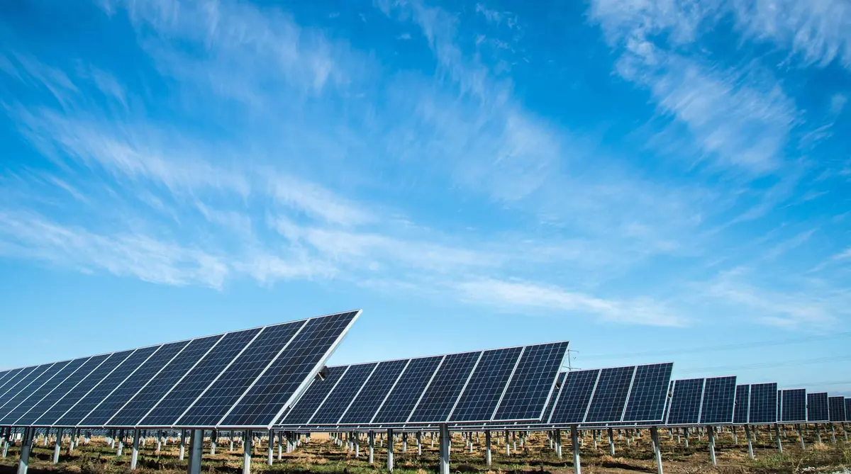 A long array of ground-mounted solar panels under a blue sky